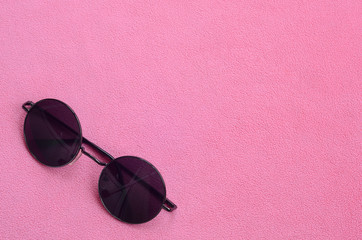 Stylish black sunglasses with round glasses lies on a blanket made of soft and fluffy light pink...