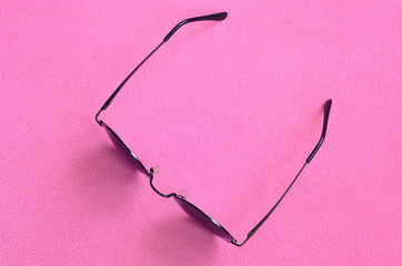 Stylish black sunglasses with round glasses lies on a blanket made of soft and fluffy light pink...