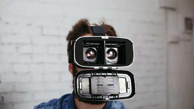 Man wearing virtual reality goggles in the office. He is opening them to show what is inside. Modern technology at work