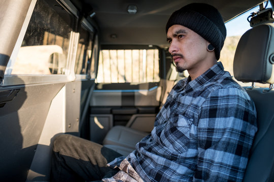 A handcuffed man sits in the back of a police vehicle,