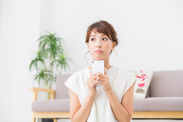 部屋でスマホを見る女性　考える