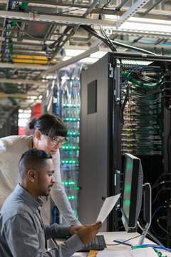Two server room technicians look at paperwork in a busy server r