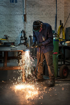 Factory worker looks down at sheet metal he is welding as sparks