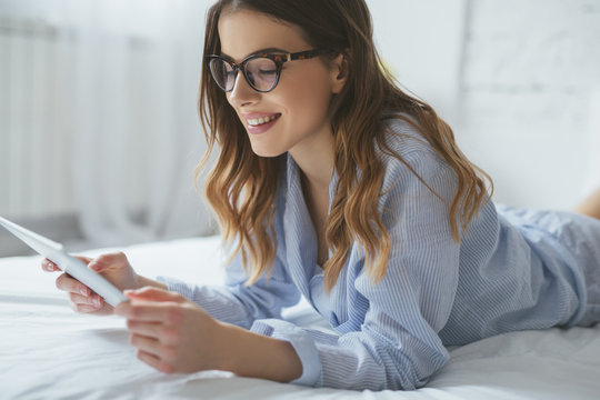 Young Woman Lying In Her Bed And Reading From Tablet