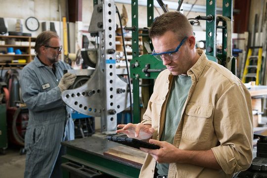 Factory worker looking at digital tablet with coworker in background