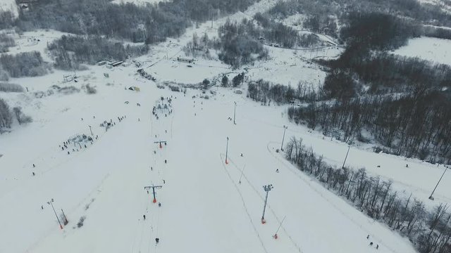 Aerial view: Skiers and snowboarders going down the slope in winter day. Skiers and snowboarders enjoying on slopes of ski resort in winter season. 4K video, aerial footage.