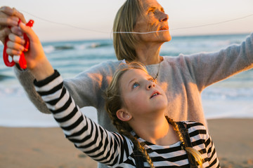Grandmother and her granddaughter flying a kite on the beach at sunset.