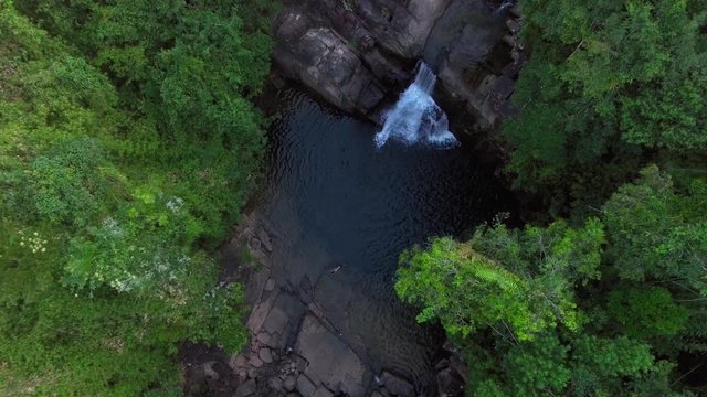 aerial shot woman swimming alone in waterfall pond in a forest