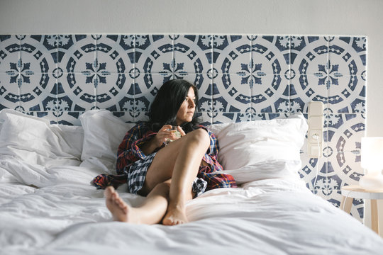 casual woman with her boyfriends clothes relaxing on a bed enjoying a cocktail