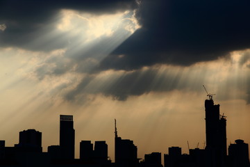silhouette cityscape with powerful sun light beaming through dark cloudy sky.