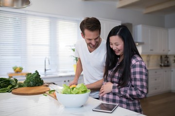 Obraz na płótnie Canvas Pregnant couple preparing salad together in the kitchen