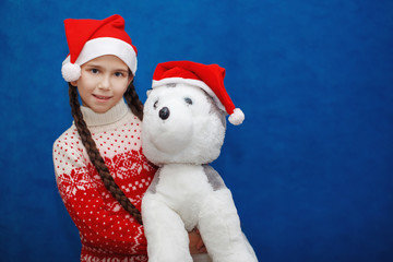 Little girl Santa celebrates Christmas with a toy dog Husky