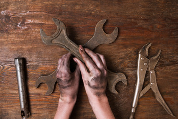 Female repairer. Woman hand holding a spanner and other tools lay on a wooden background. Feminism...