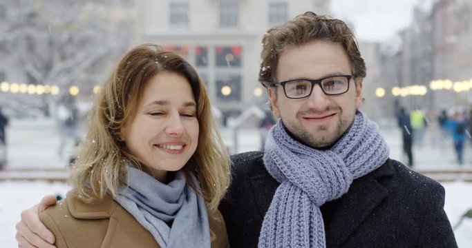 Portrait of the attractive couple of middle age hagging and smiling in front of the camera in the town on snowy day. Close up. Outdoors