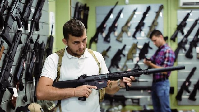 positive young man choosing air weapon in military shop