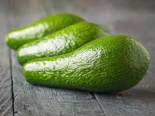 Three avocados stacked in a row on a dark rustic table.