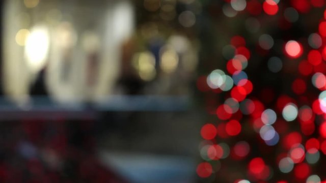 Defocused people passing stores and Christmas tree decorated with red lights in shopping mall during winter holiday season in time lapse video