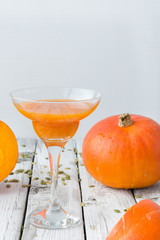 A wineglass of fresh pumpkin juice with pumpkins and seeds