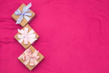 Three gift boxes tied with satin coloured ribbon on a pink background a Red heart.