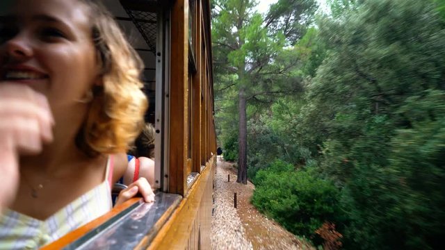 Young happy woman enjoys ride with old wooden train through beautiful mountain landscape nature in 4k