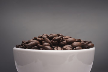 Coffee beans in a white cup with grey background.Close up shot with selective focus.