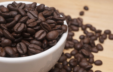 Coffee beans in a white cup with spilled seeds on the wooden board.Close up shot with selective focus.