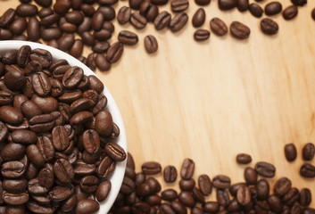 Coffee beans in a white cup with spilled seeds on the wooden board.Close up shot with selective focus.