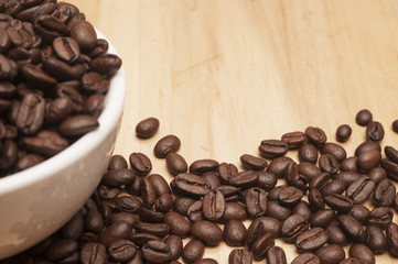 Coffee beans in a white cup with spilled seeds on the wooden board.Close up shot with selective focus.