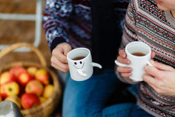 Hands close up of Couple drinking a hot drink from cups at picnic sitting on a blanket. Boy and Girl in love sitting on a picnic plaid in a park, drinking coffee and enjoying their day out in nature