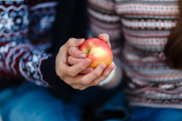 Fototapeta na wymiar Hands close up of young couple holding an Apple in warm sweaters and holds a picnic sitting on a blanket. Beautiful young couple holding a red Apple.