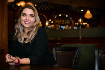 Young elegant plus size woman in cozy atmosphere restaurant. Lady wait on a date in romantic mood. Portrait in deep vintage tones