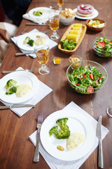Broccoli on plates, salad in bowl and drinks in wineglasses on served wooden table