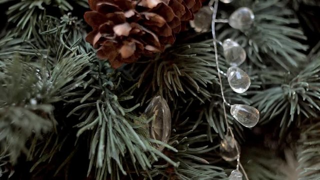 Christmas decoration of silver spangled feather, crystal garland and pine cone on green fir tree branches. Pan and tilt, close up