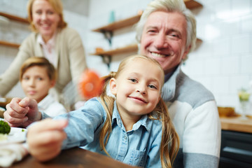 Fototapeta premium Adorable girl on grandfather hands looking at camera by table during family breakfast