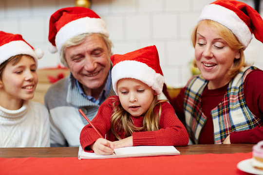 Senior couple and their grandson looking at little girl with crayon drawing xmas picture in notepad
