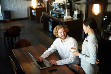 Happy man looking at waitress bringing him cup of coffee while he networking in cafe