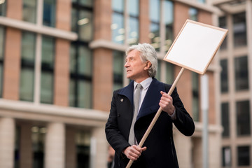 Senior businessman holding placard of protest during demonstration against unjust issue