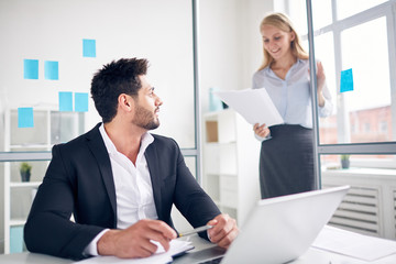 Businessman listening to secretary reading data in papers while standing in office door