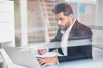 Fototapeta premium Busy young analyst looking through online statistics and writing some things in notebook