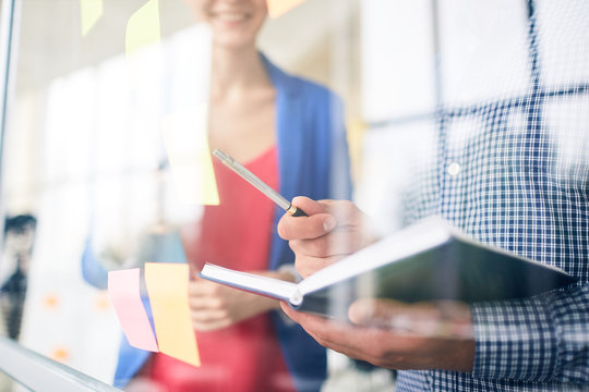 Manager with open notebook and pen pointing at one of reminders on noteboard