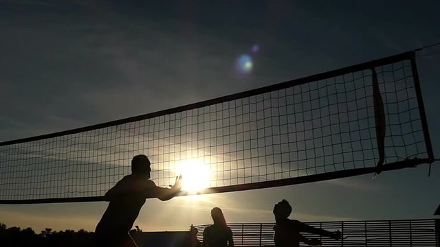 Sportive people playing volleyball at a network at sunset in slow motion