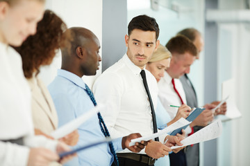Fototapeta premium Two intercultural managers discussing data on papers among colleagues while preparing their financial reports