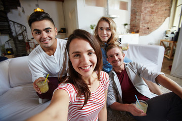 Happy girl and her friends looking at camera with smiles while making selfie