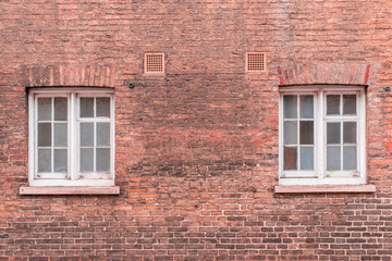 Two white wooden sash windows on a restored red brick wall of a Victorian house residential building