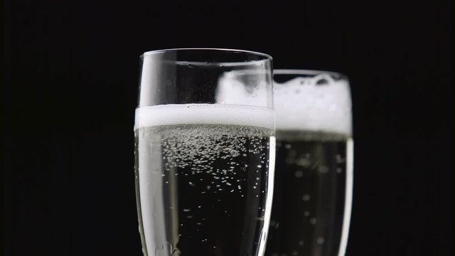 Filled with two glasses of champagne with white bubbles on a black background. Close up