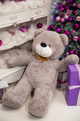 Toy gray teddy bear gift near a smart Christmas tree at Christmas