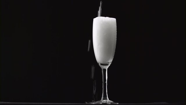 Champagne is poured into the misted glass on a thin stalk. Black background