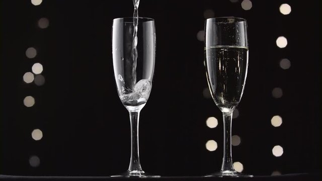 Champagne being poured into two transparent glass. Bokeh blinking black background