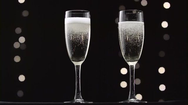 Two transparent glass of chilled sparkling wine. Bokeh blinking black background