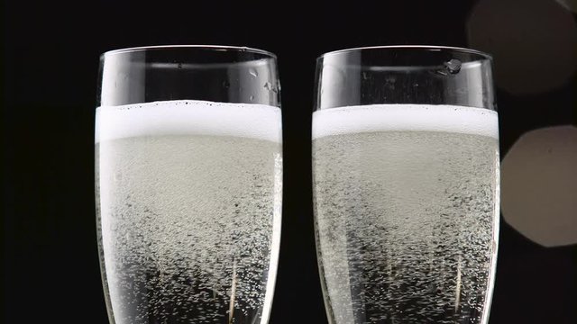 Two transparent glass of chilled champagne. Bokeh blinking black background. Close up
